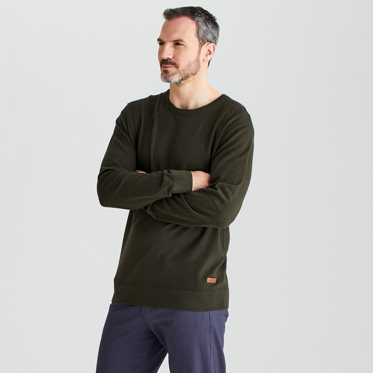 Man wearing a dark green sweater with a small logo on a light gray background