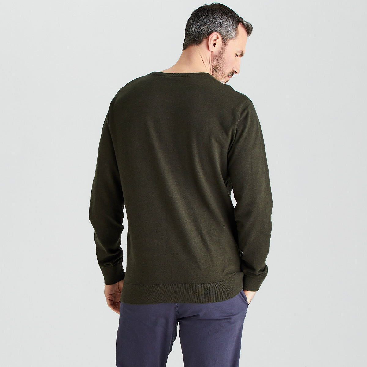 Man wearing a green sweater and dark pants on a light gray background