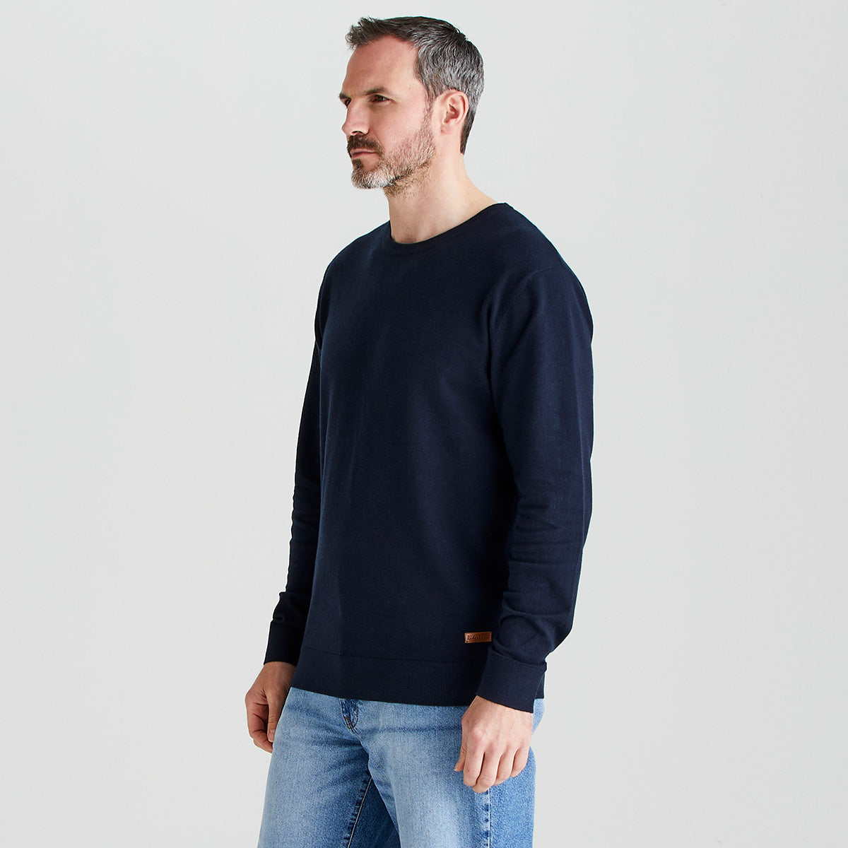 Man wearing a navy sweater and light blue jeans on a plain background