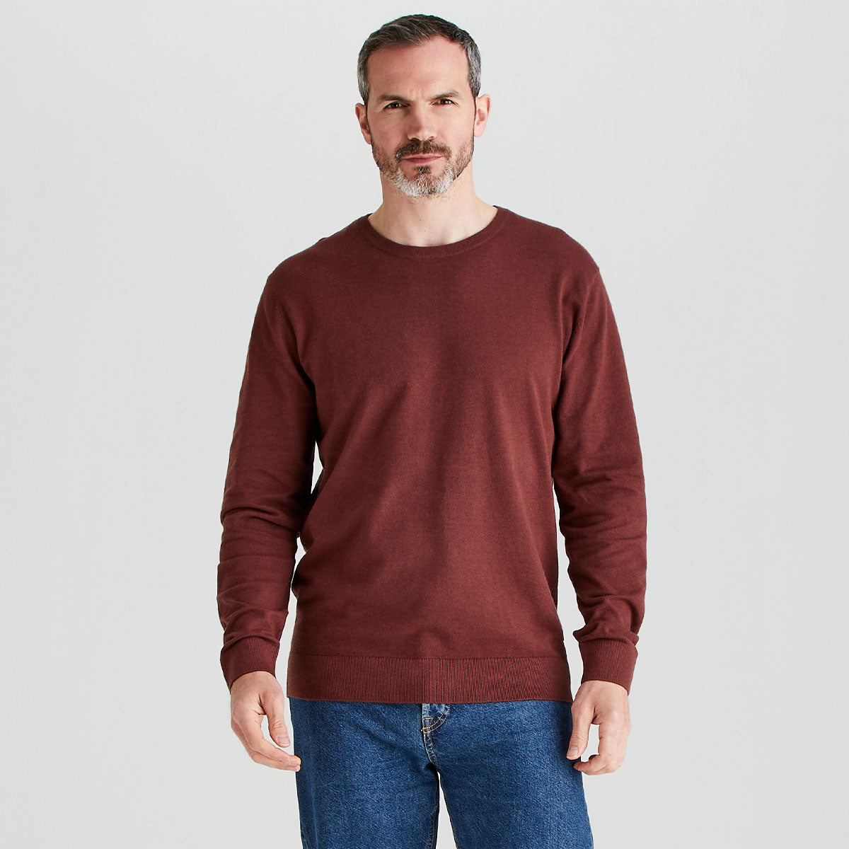 Man wearing a brown sweater and blue jeans on a light gray background