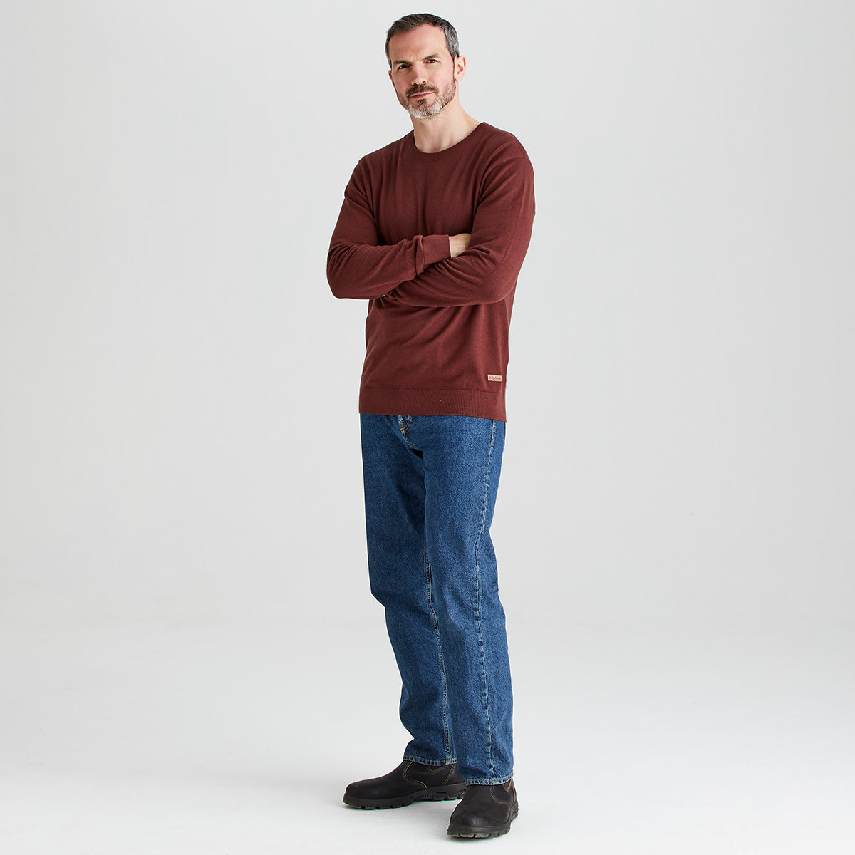 Man wearing a brown sweater and blue jeans standing against a white background