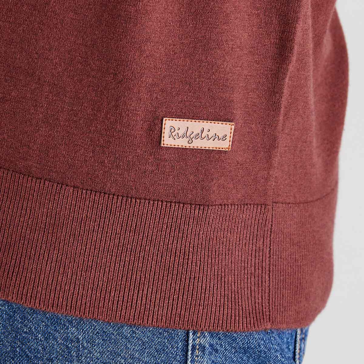 Close-up of a maroon sweater with a brand label on a light gray background