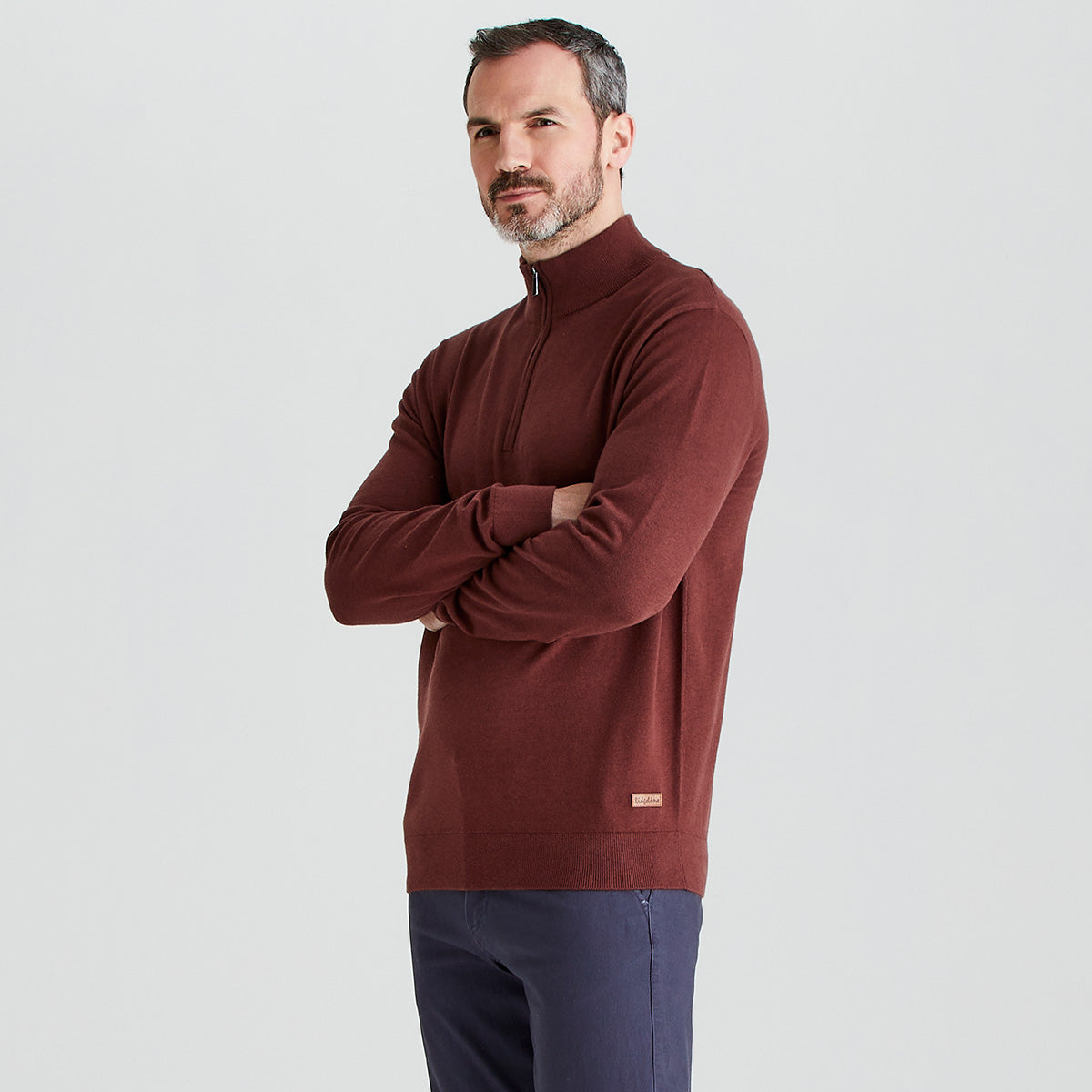 Man wearing a brown sweater with a small logo on a light gray background