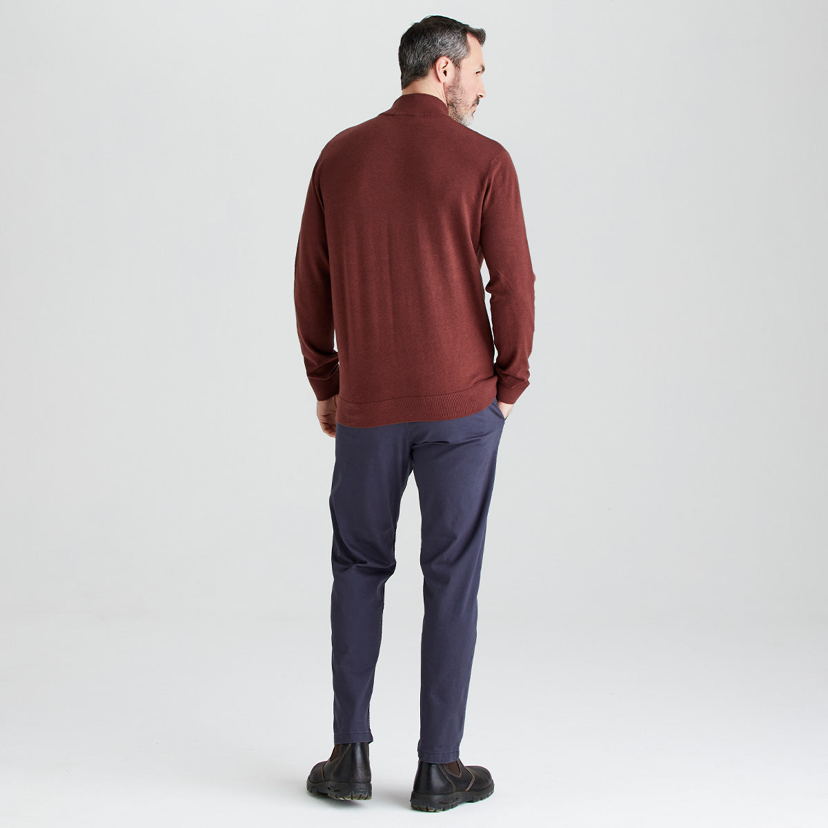 Man wearing a brown sweater and dark pants on a white background