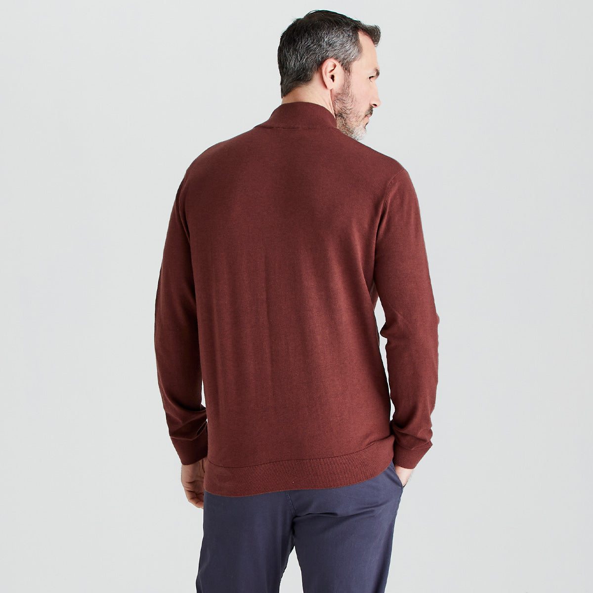 Man wearing a brown sweater and dark pants on a light gray background
