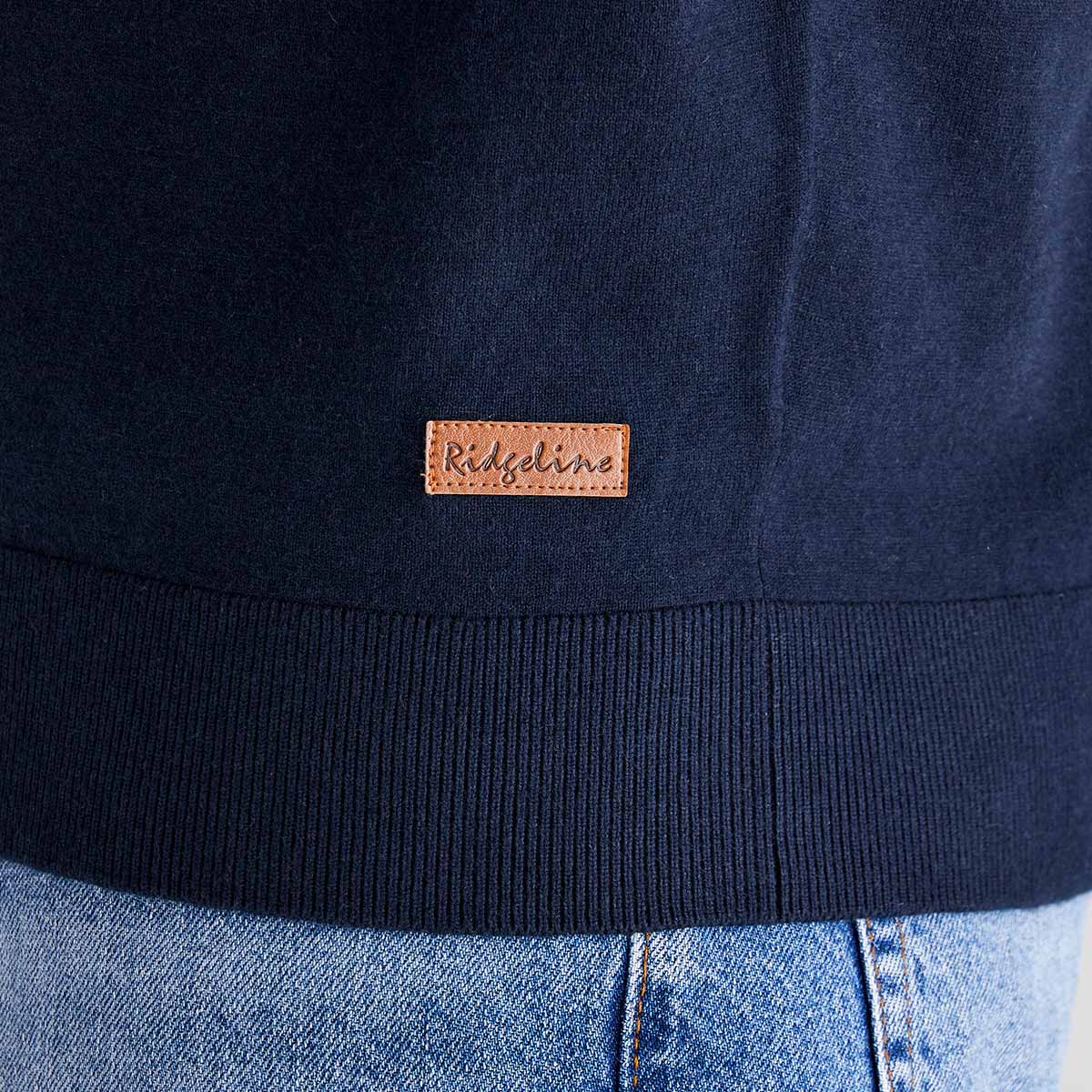 Navy blue sweatshirt with a leather-like brand label on the chest, worn with light blue jeans.