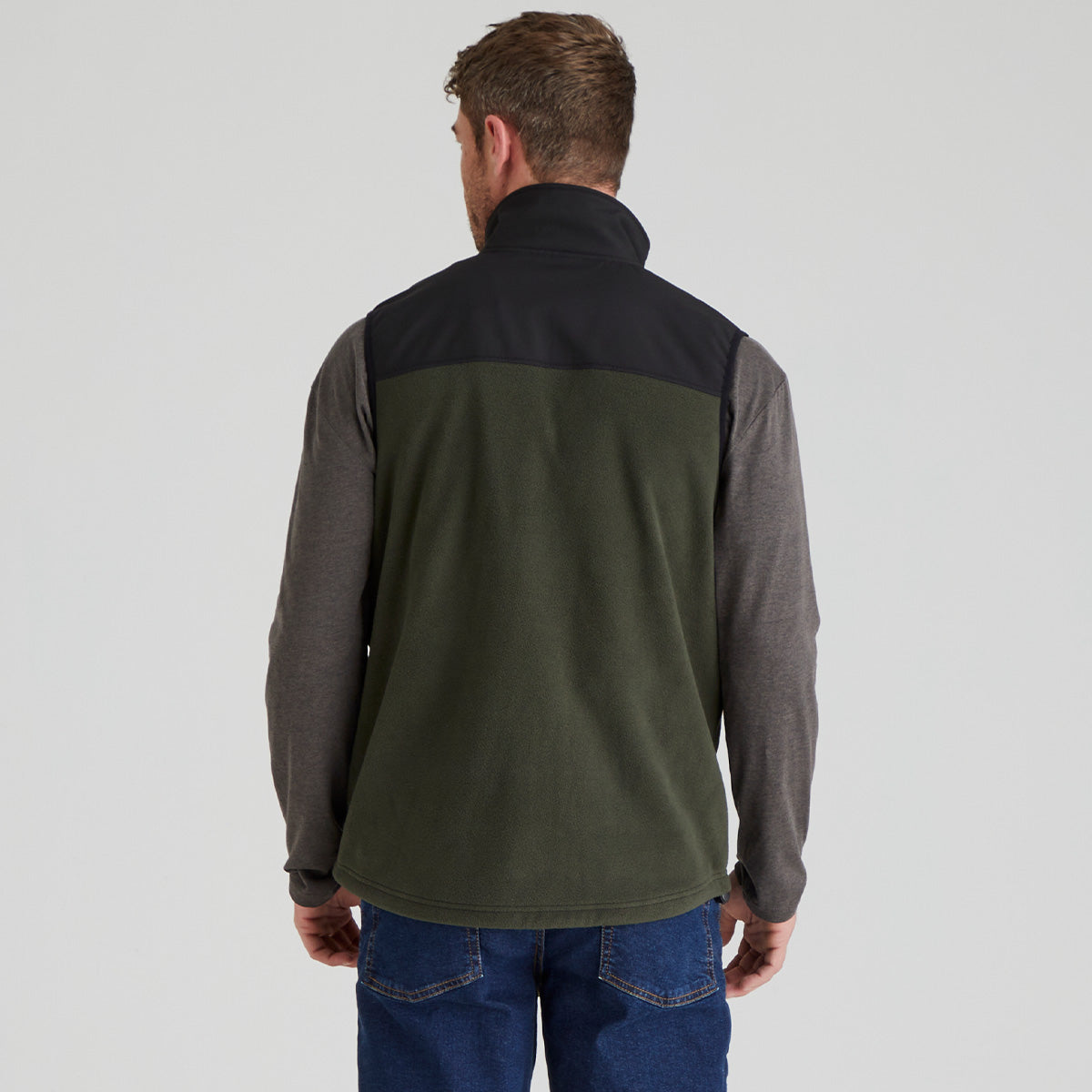 back view of man wearing a two-tone jacket with black and green sections on a light grey background
