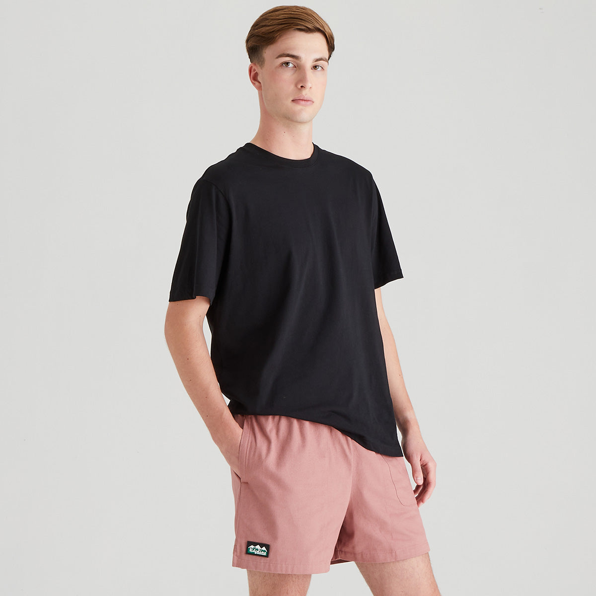 Person wearing a black t-shirt and pink shorts on a light gray background