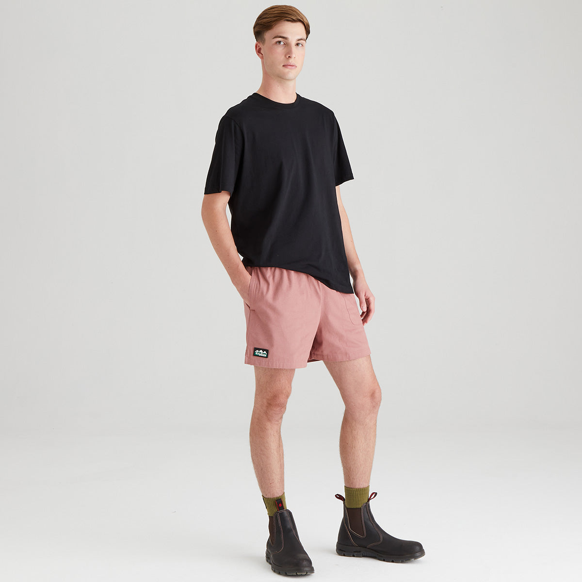 Person wearing a black t-shirt and pink shorts on a white background