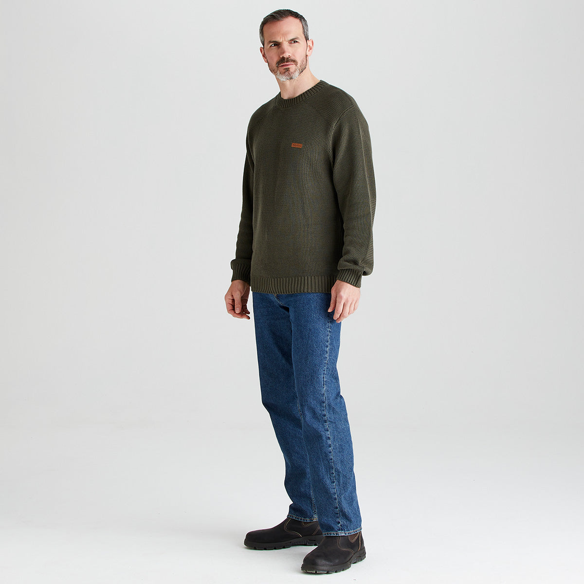 Man wearing a green sweater and blue jeans on a white background
