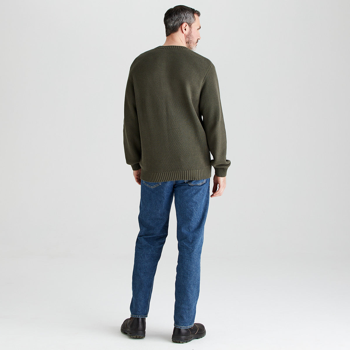 Man wearing a green sweater and blue jeans on a white background