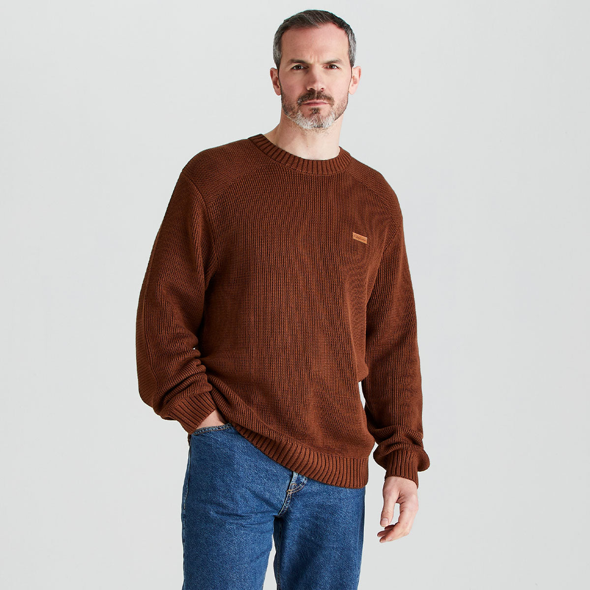 Man wearing a brown sweater and blue jeans on a light gray background