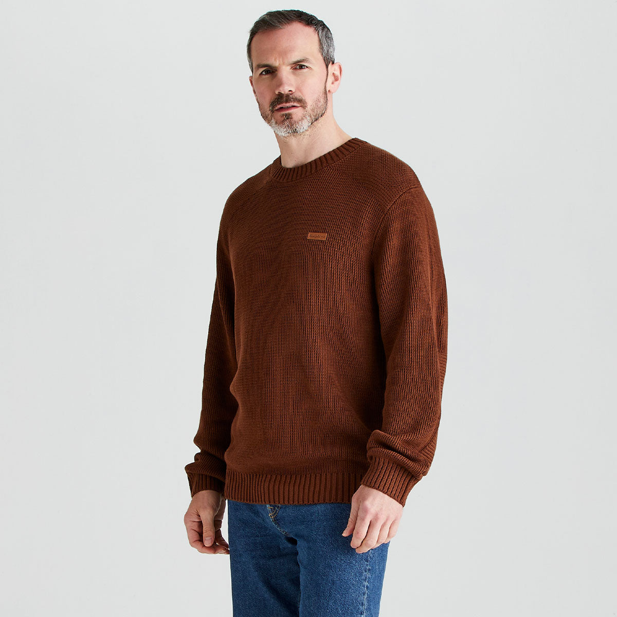 Man wearing a brown sweater and blue jeans on a light gray background