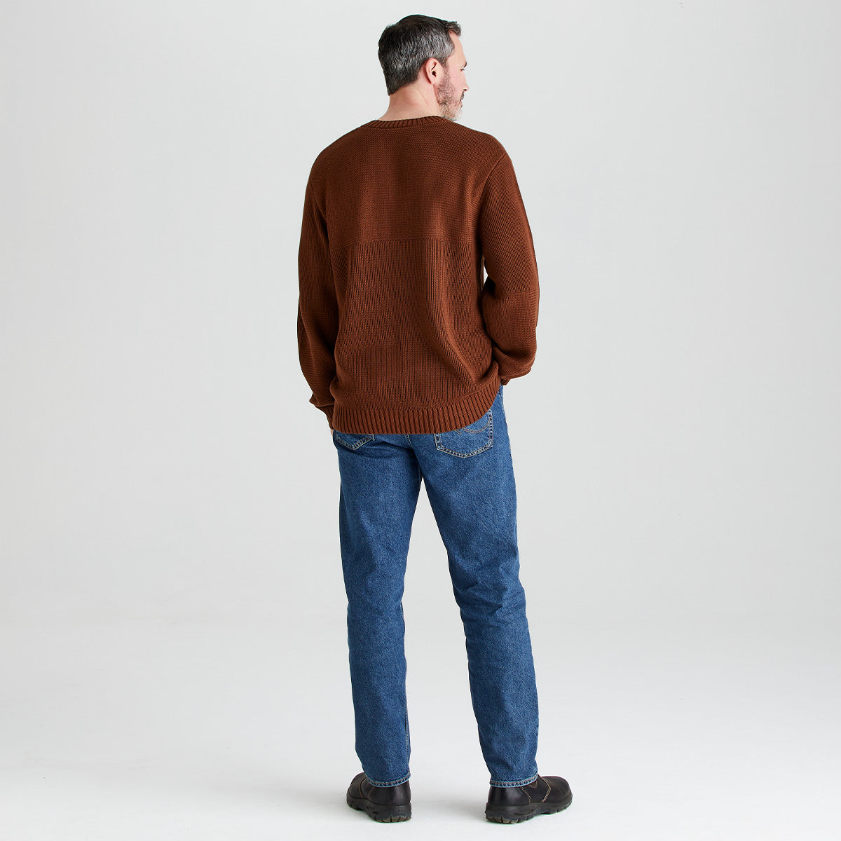 Man wearing a brown sweater and blue jeans on a light gray background