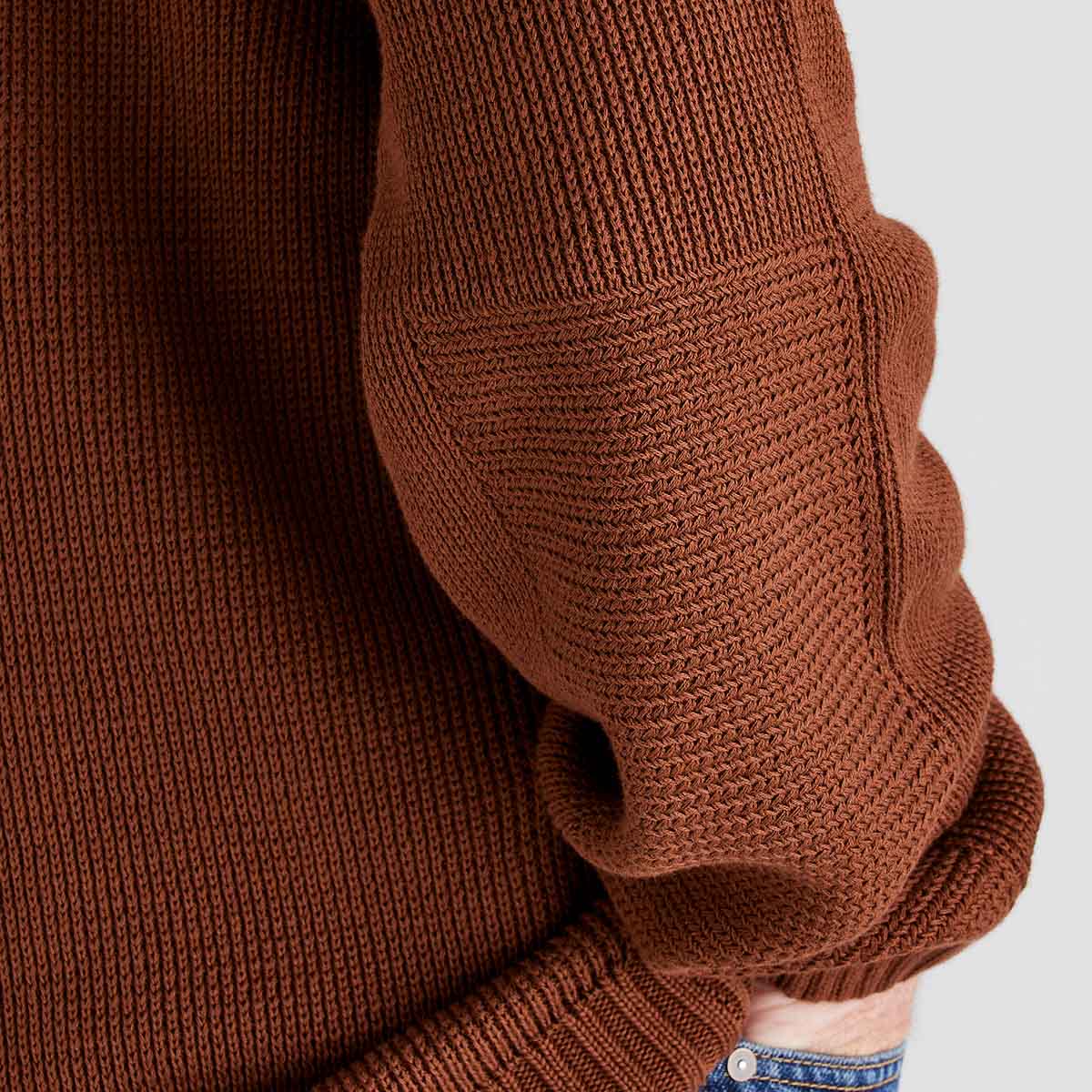Close-up of a brown knitted sweater sleeve on a light gray background