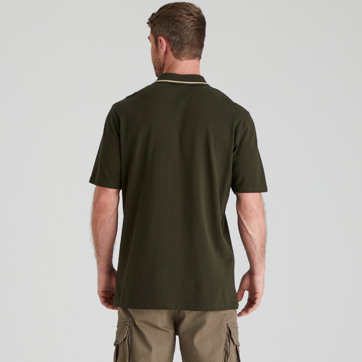 back view of man wearing a green polo shirt and beige cargo pants on a light grey background