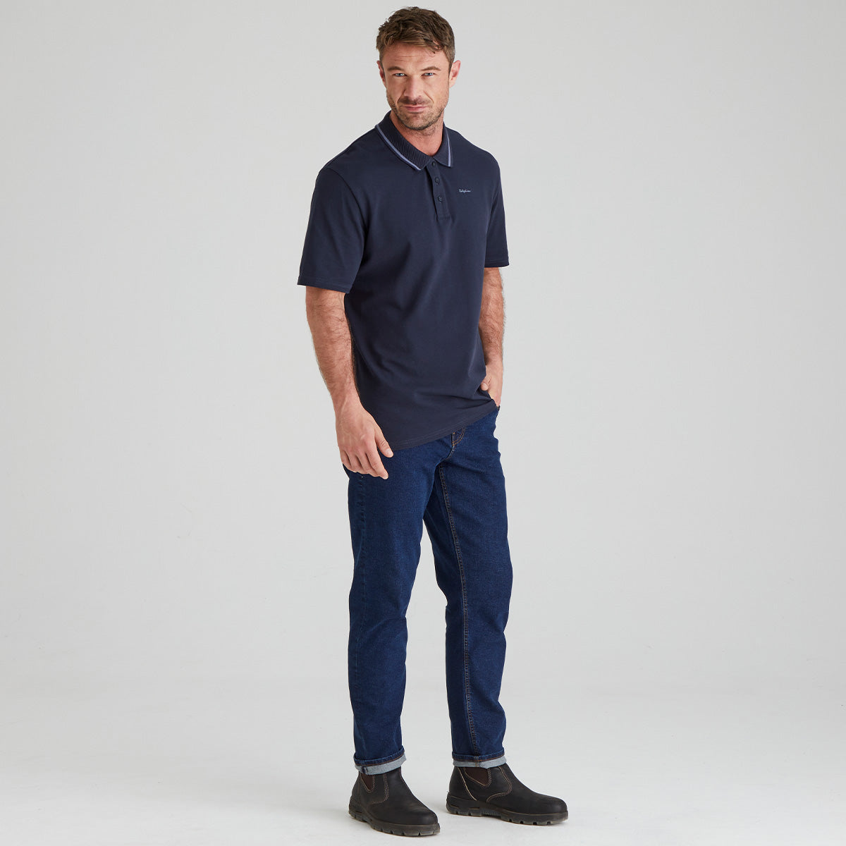 Man wearing a navy polo shirt and pants on a light gray background