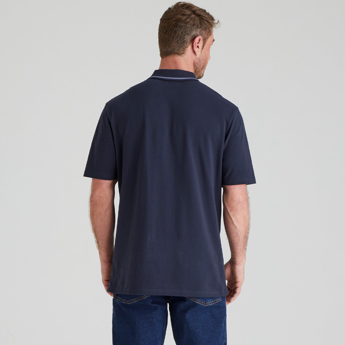 back view of man wearing a navy blue polo shirt on a light grey background