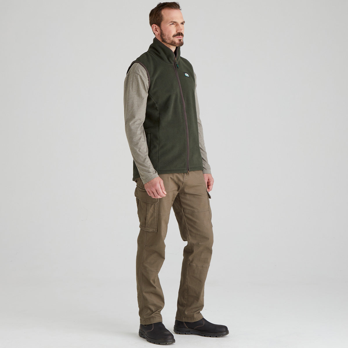 Man wearing a green fleece gilet and brown pants on a white background