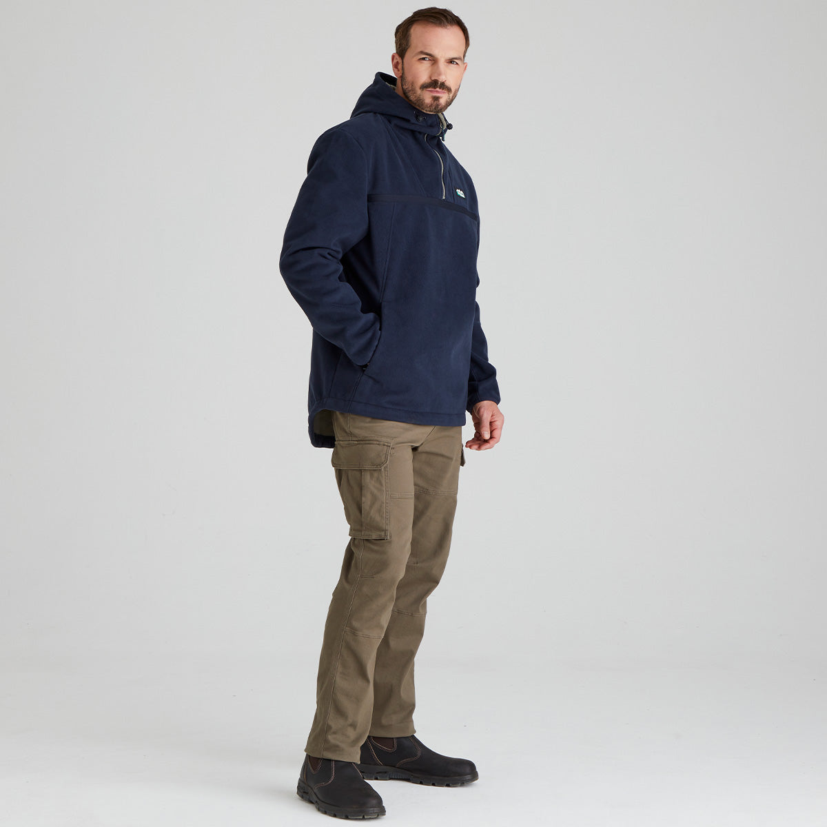 Man wearing a navy windproof fleece jacket and brown pants on a light grey background