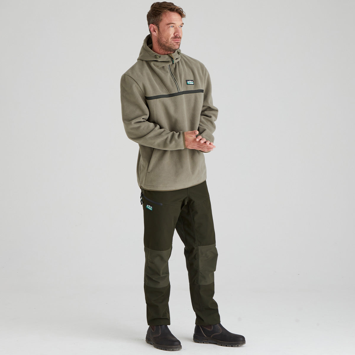 Man wearing a green pullover with a hood and matching pants on a light gray background