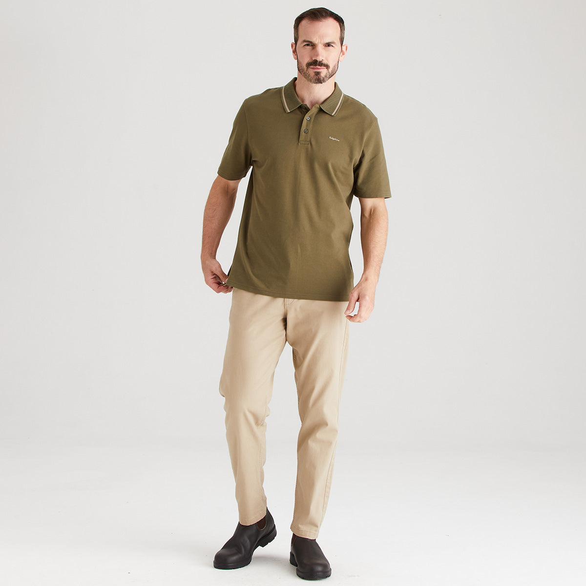 Man wearing a green polo shirt and beige pants on a white background