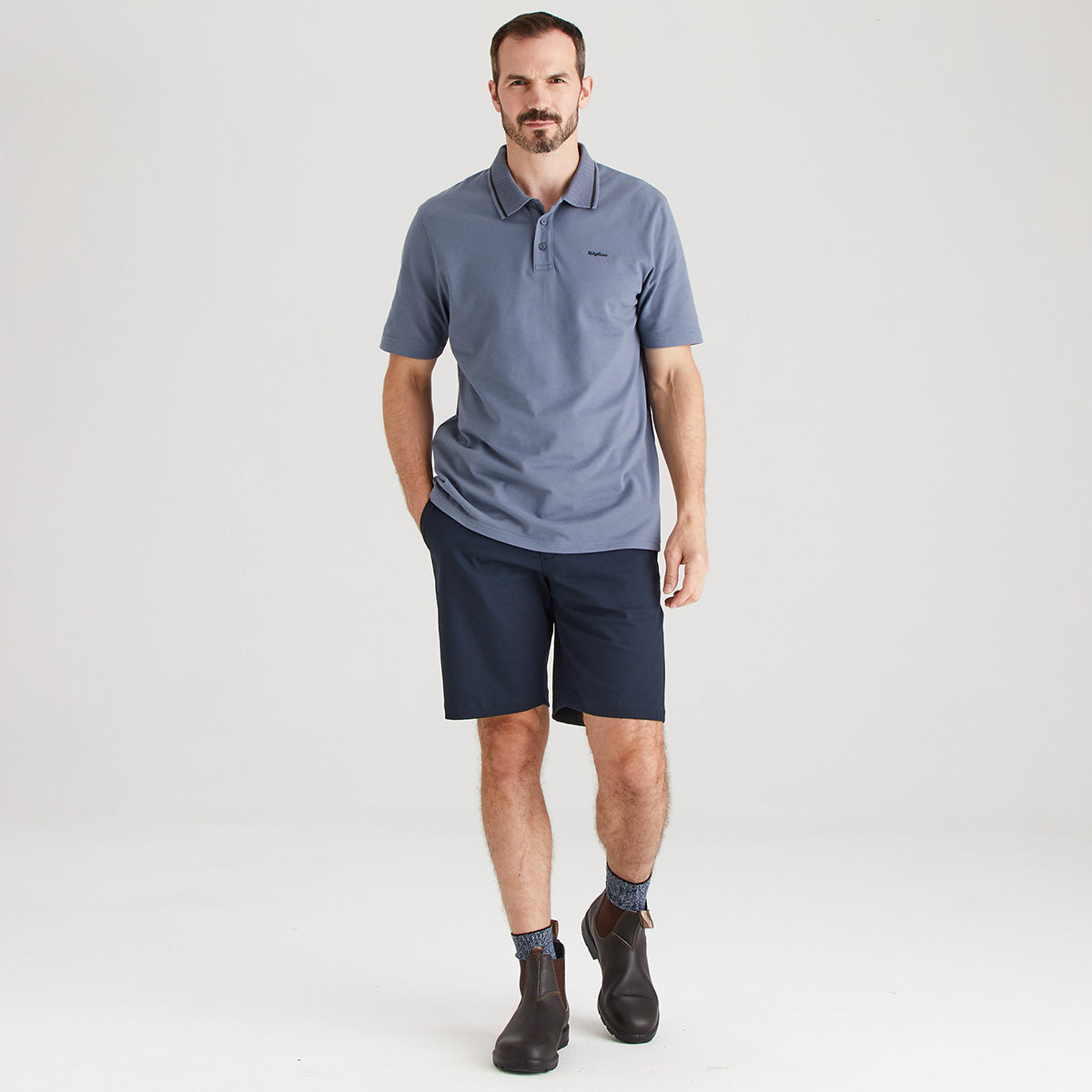 Man wearing a blue polo shirt and navy shorts on a white background