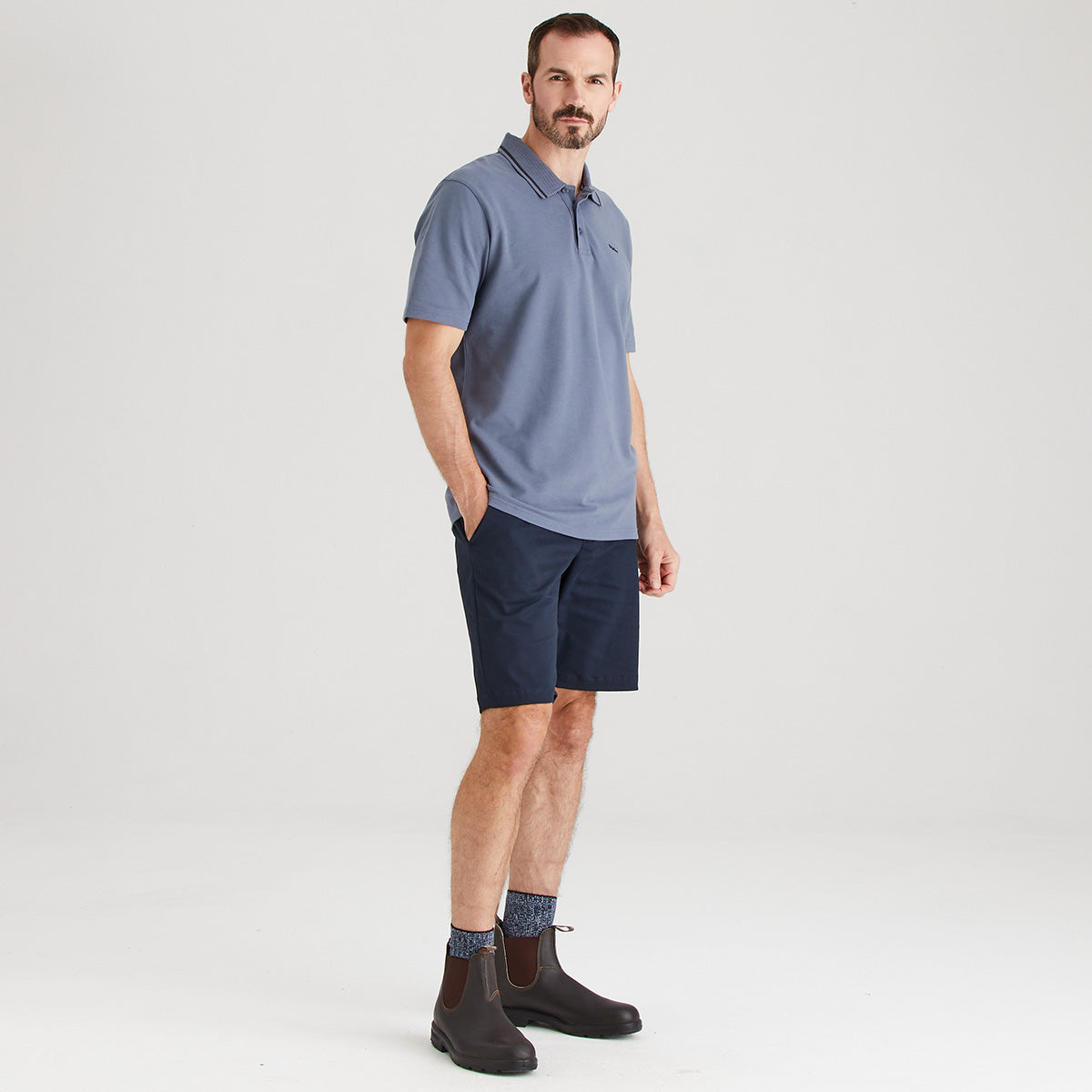 Man wearing a blue polo shirt and navy shorts on a white background