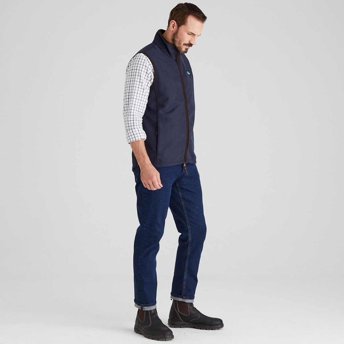 Man wearing navy windproof fleece gilet with checked shirt & jeans