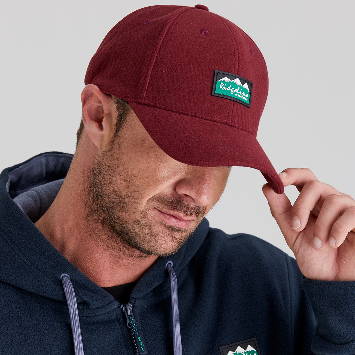 man wearing maroon hat holding the visor while posing