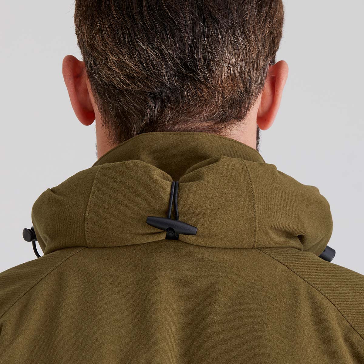 Person wearing a green jacket showing a rolled up hood with a plain background