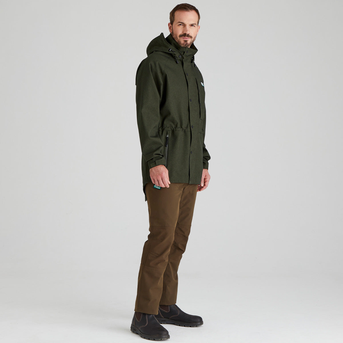 Man wearing a green raincoat and brown pants on a light gray background