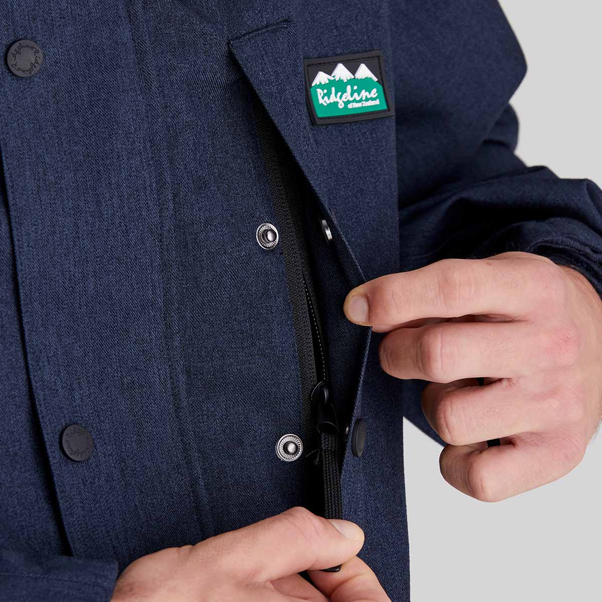 Navy blue jacket with a ridgeline clothing brand logo on the chest, being zipped by a person.