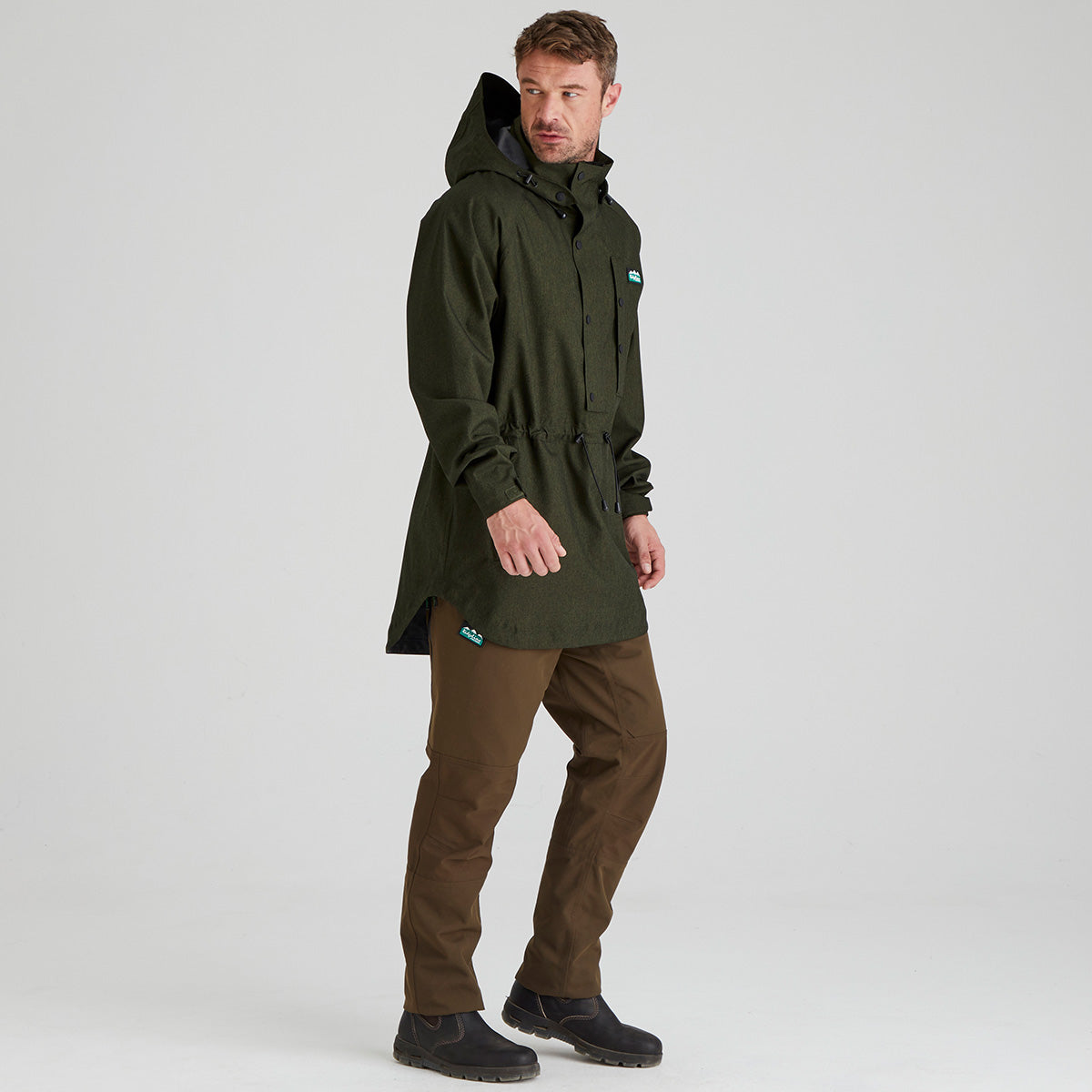 man wearing a green waterproof smock and brown pants on a white background