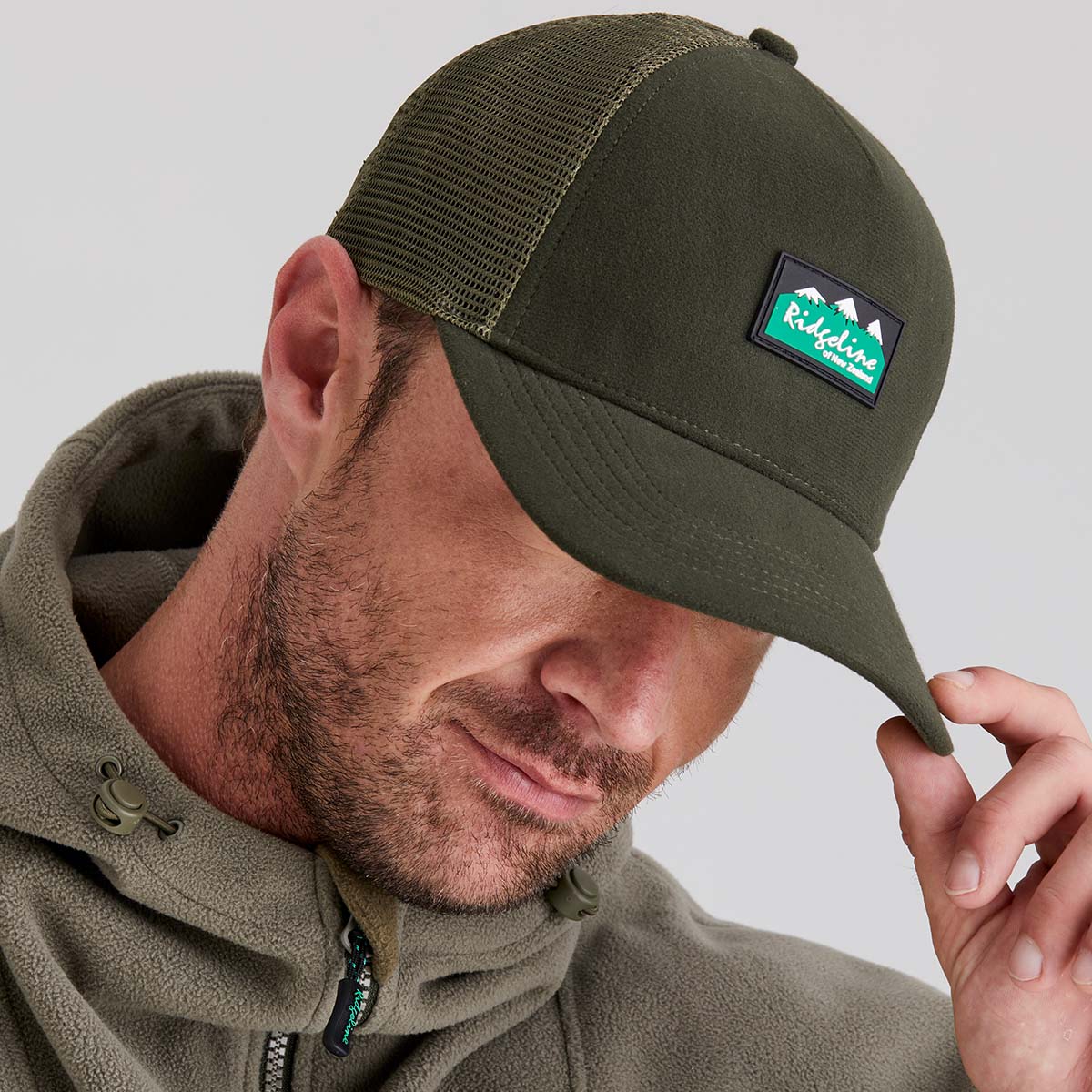 Man wearing a green cap with a brand logo on a light gray background