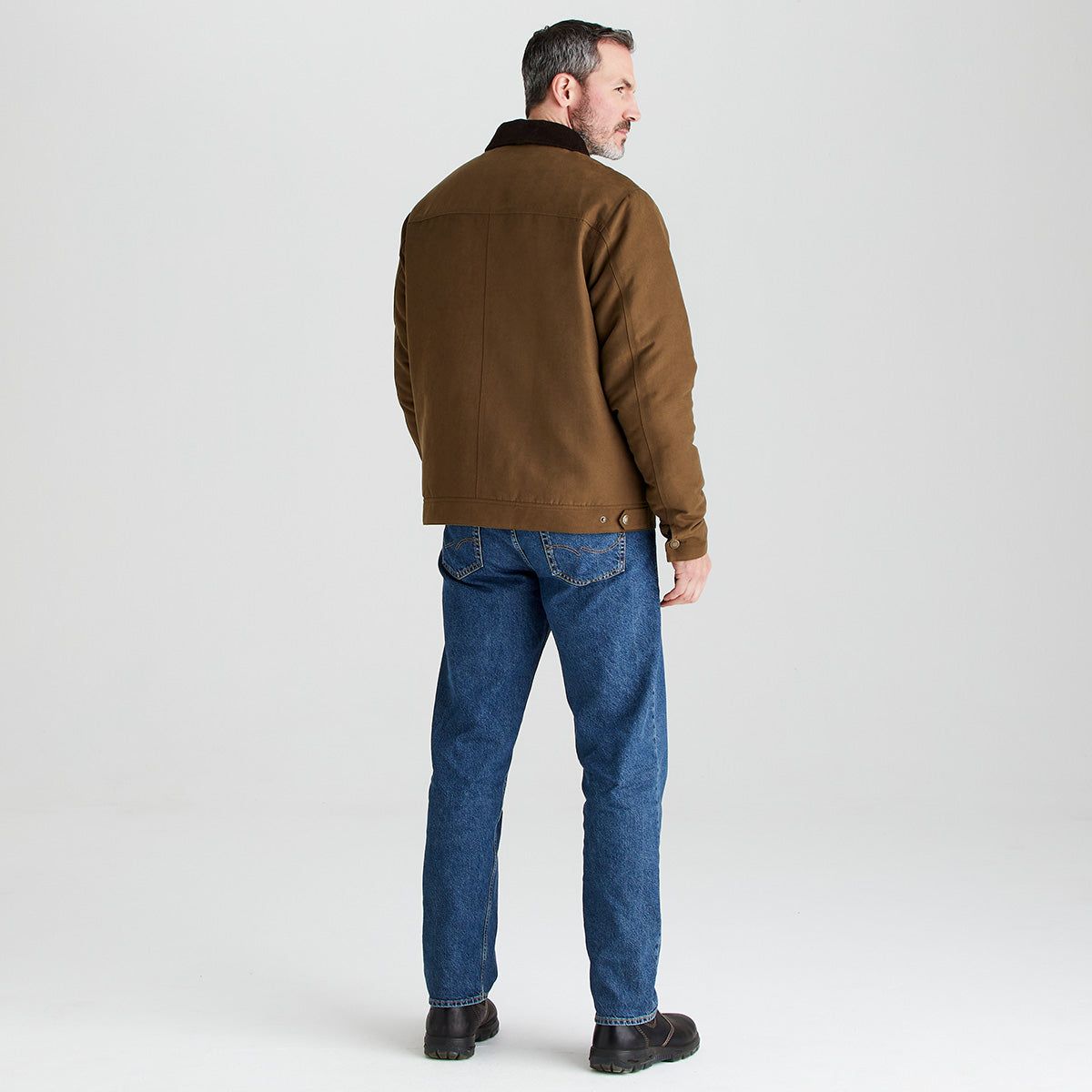 Man wearing a brown jacket and blue jeans on a light gray background
