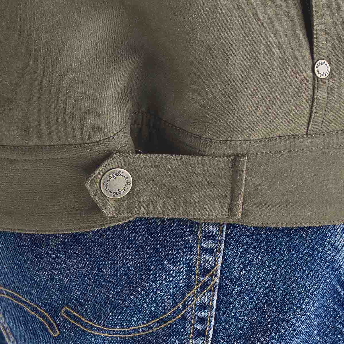 Close-up detail of an olive-green jacket hem showing an adjustable side tab with a metal snap fastener. The image highlights the jacket’s stitching, fabric texture, and hem construction, with blue denim jeans visible beneath.