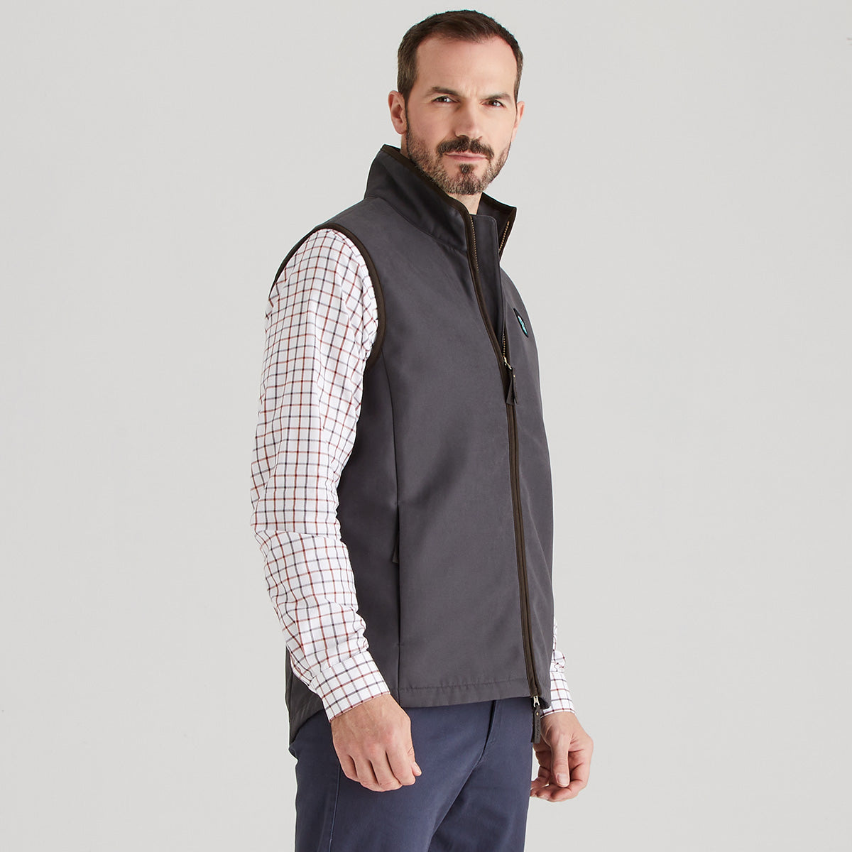 Man wearing a grey vest over a checkered shirt on a light grey background