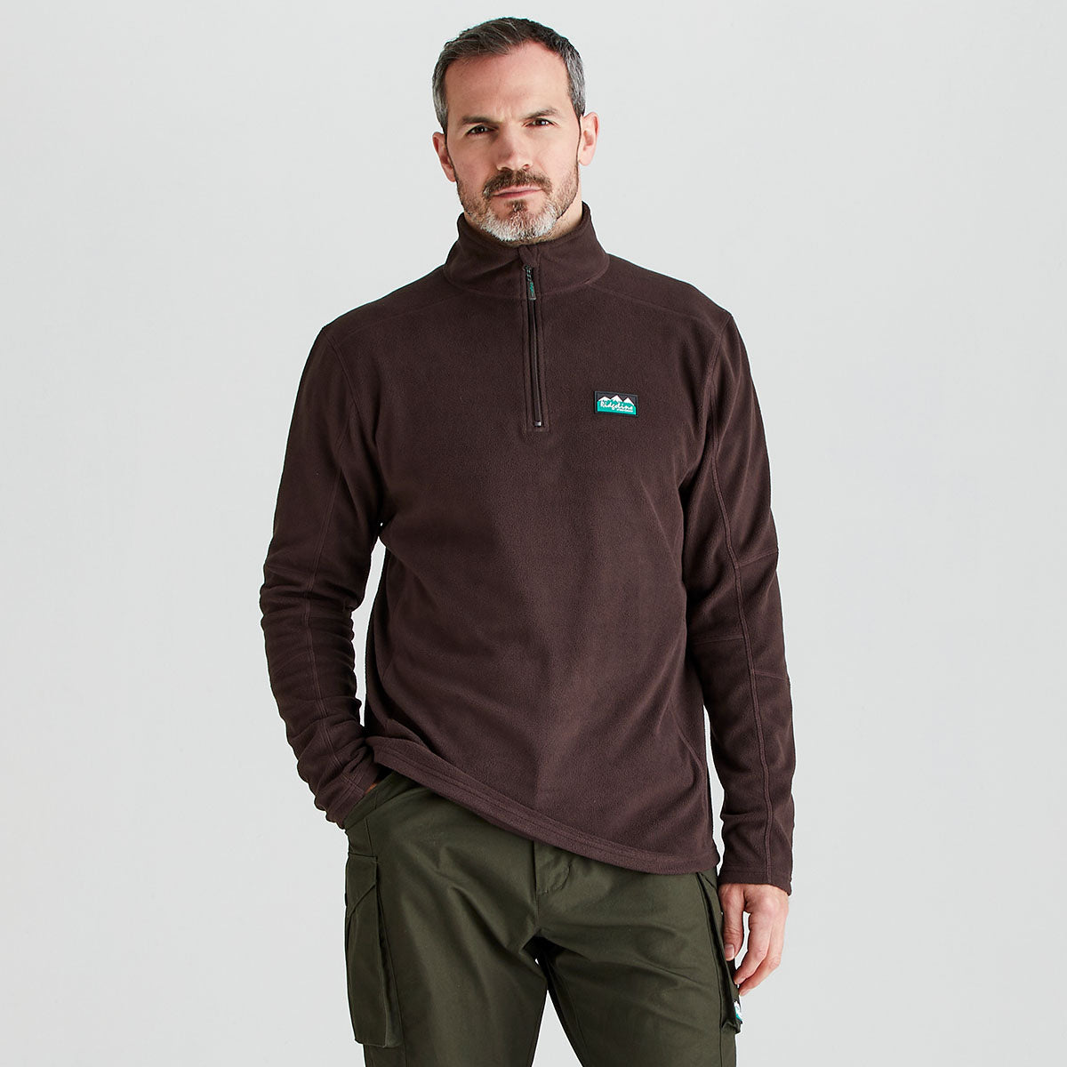 Man wearing a Ridgeline brown or burgundy fleece pullover with a logo on a light gray background