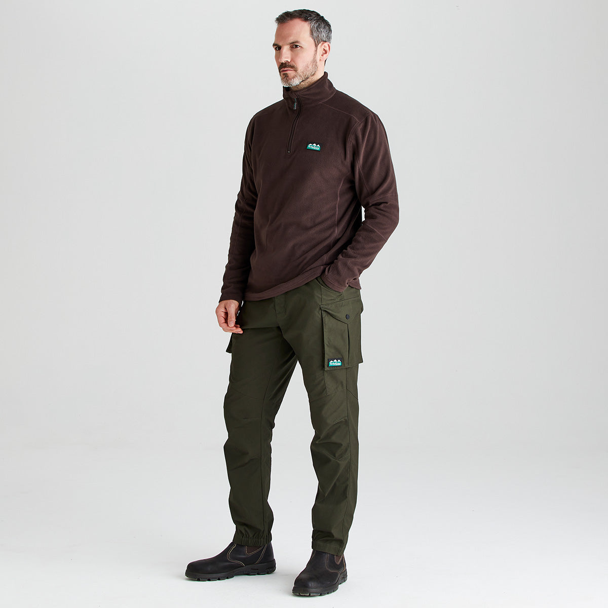 Man wearing a brown fleece jacket and green cargo pants on a white background