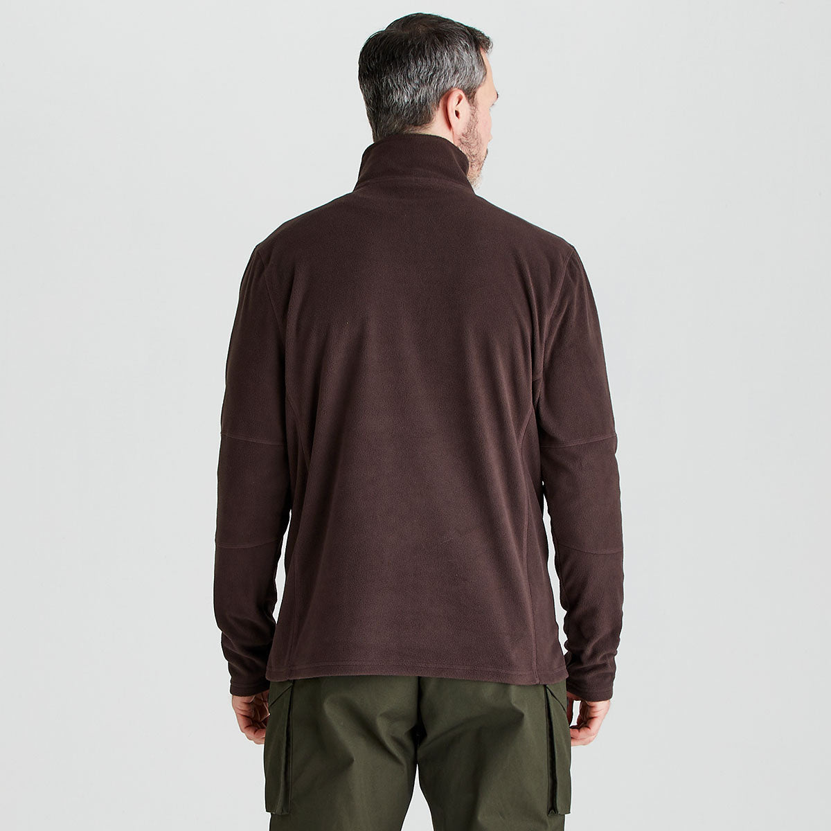 Man wearing a brown fleece jacket and green pants on a light gray background