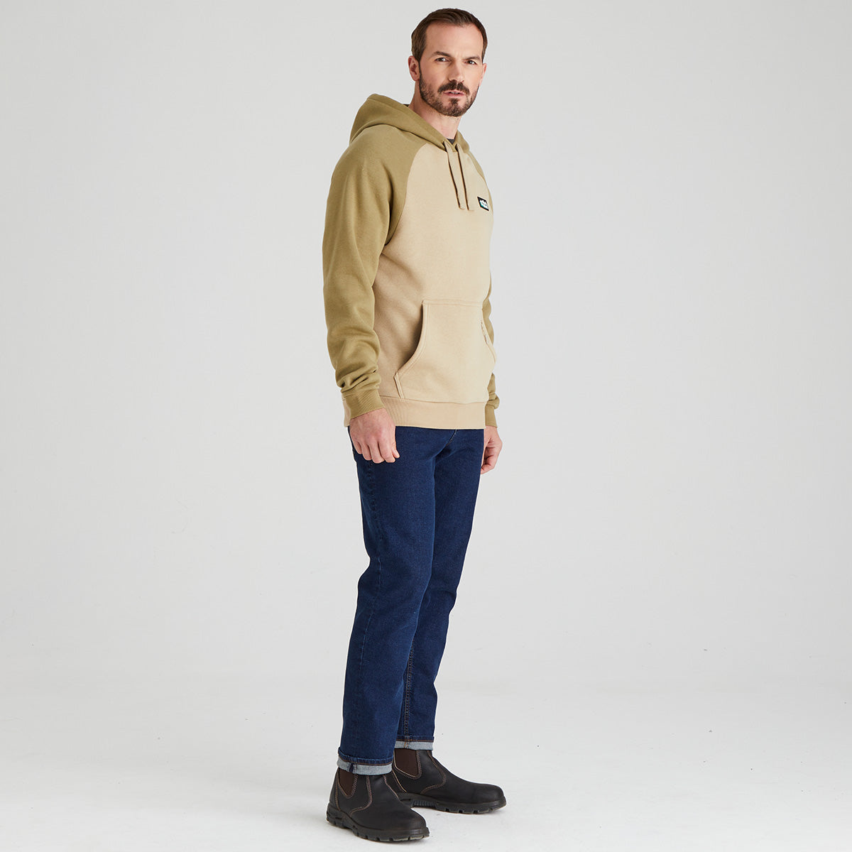 Man wearing a beige hoodie and blue jeans on a white background