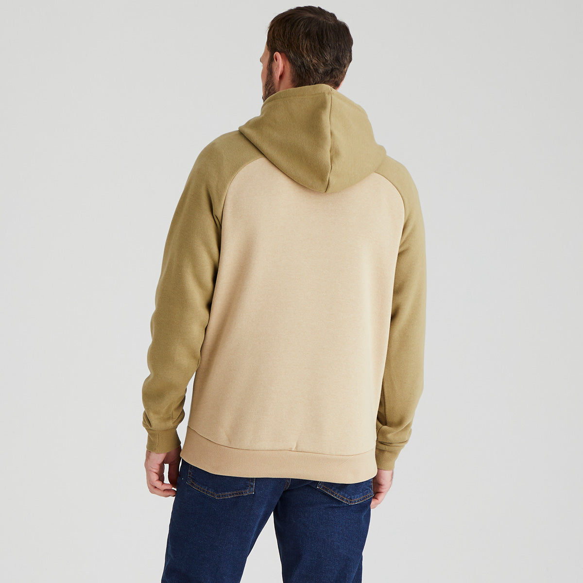back view of man wearing a beige and green hoodie on a light grey background