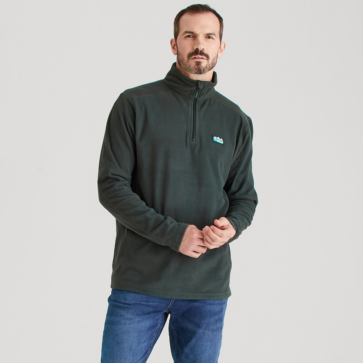 Man wearing a dark green pullover with a logo on a light gray background