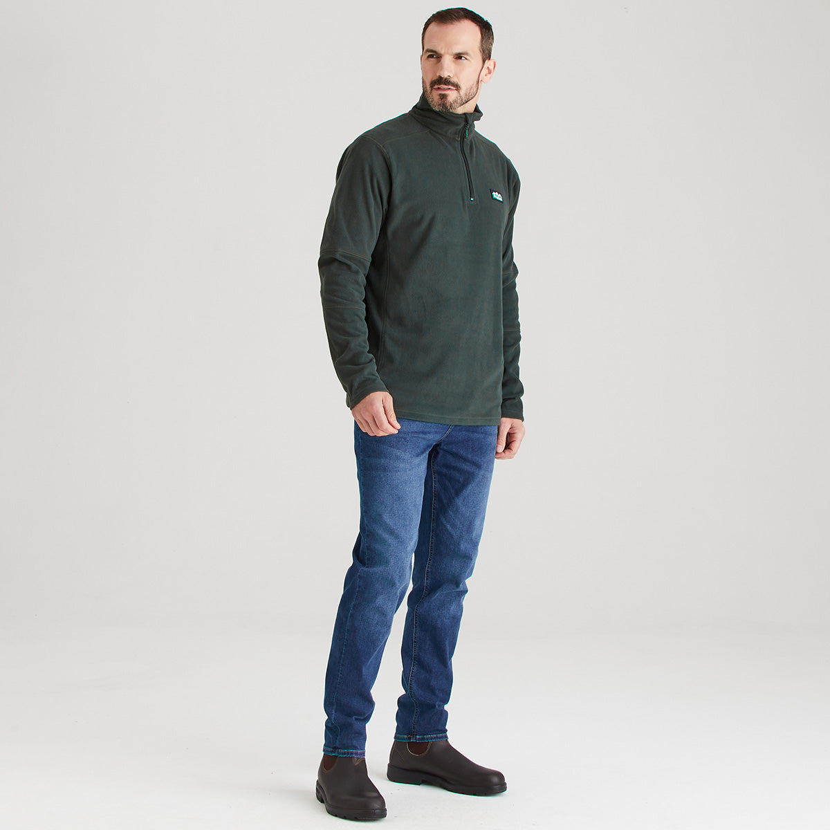 Man wearing a green fleece pullover and blue jeans on a white background