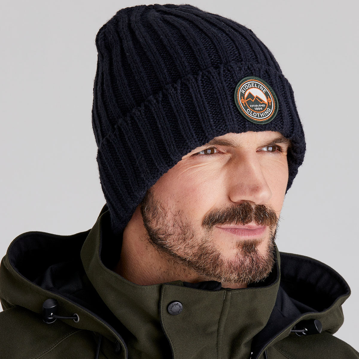 Man wearing a navy knit beanie with a logo on a grey background