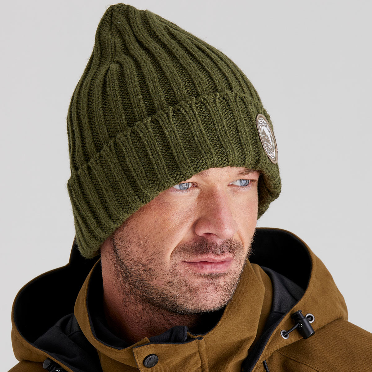 Man wearing a green knit beanie with a brand logo on a grey background