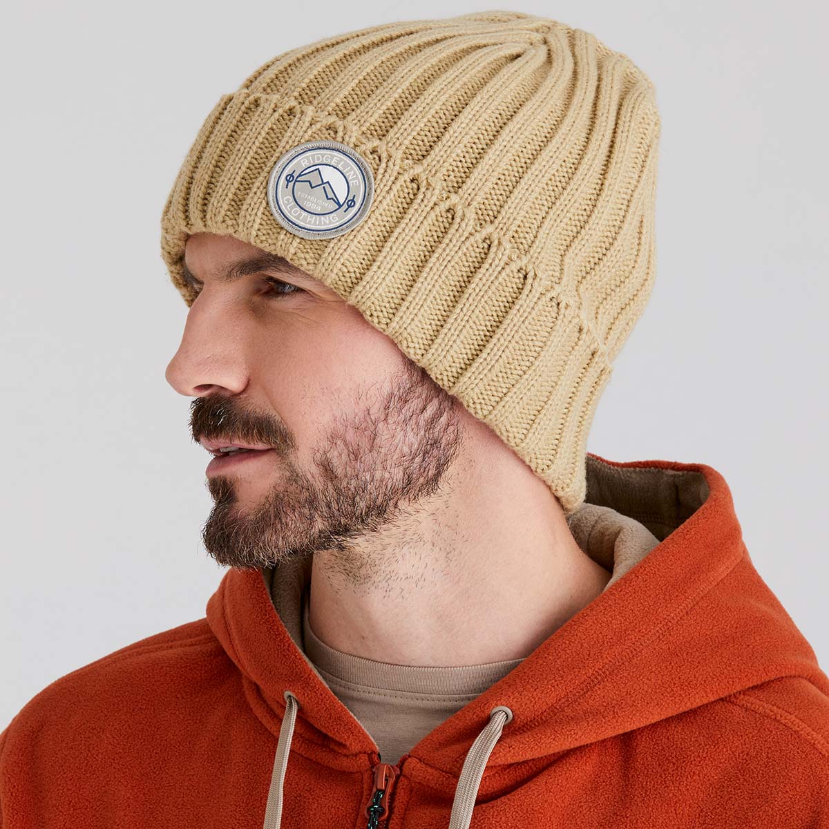 Man wearing a beige knit beanie with a logo on a light grey background