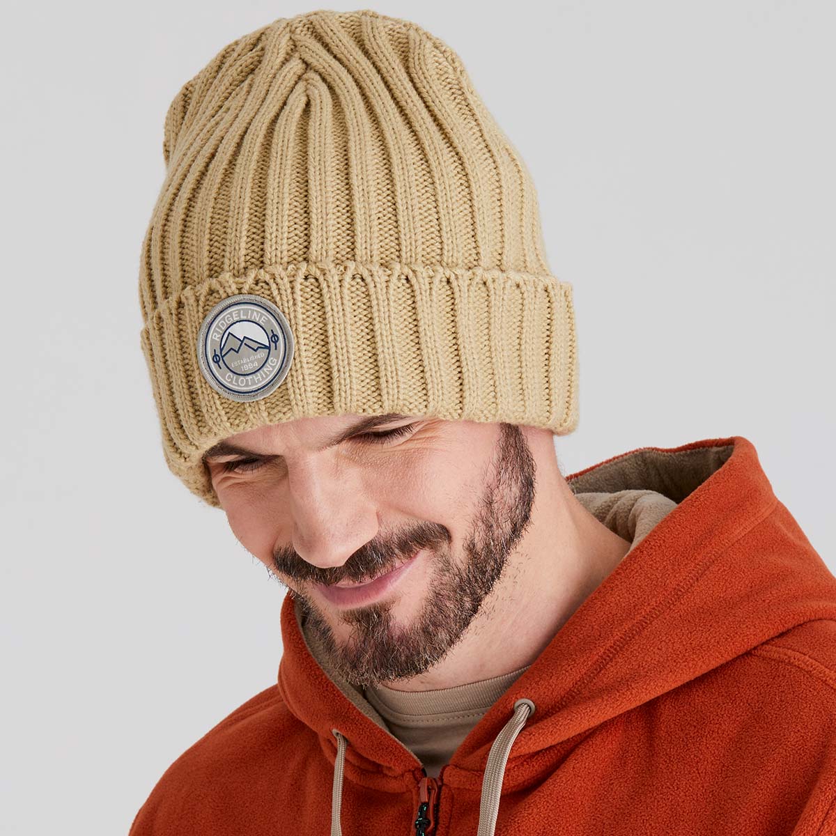 Man wearing a beige knit beanie with a logo on a light gray background