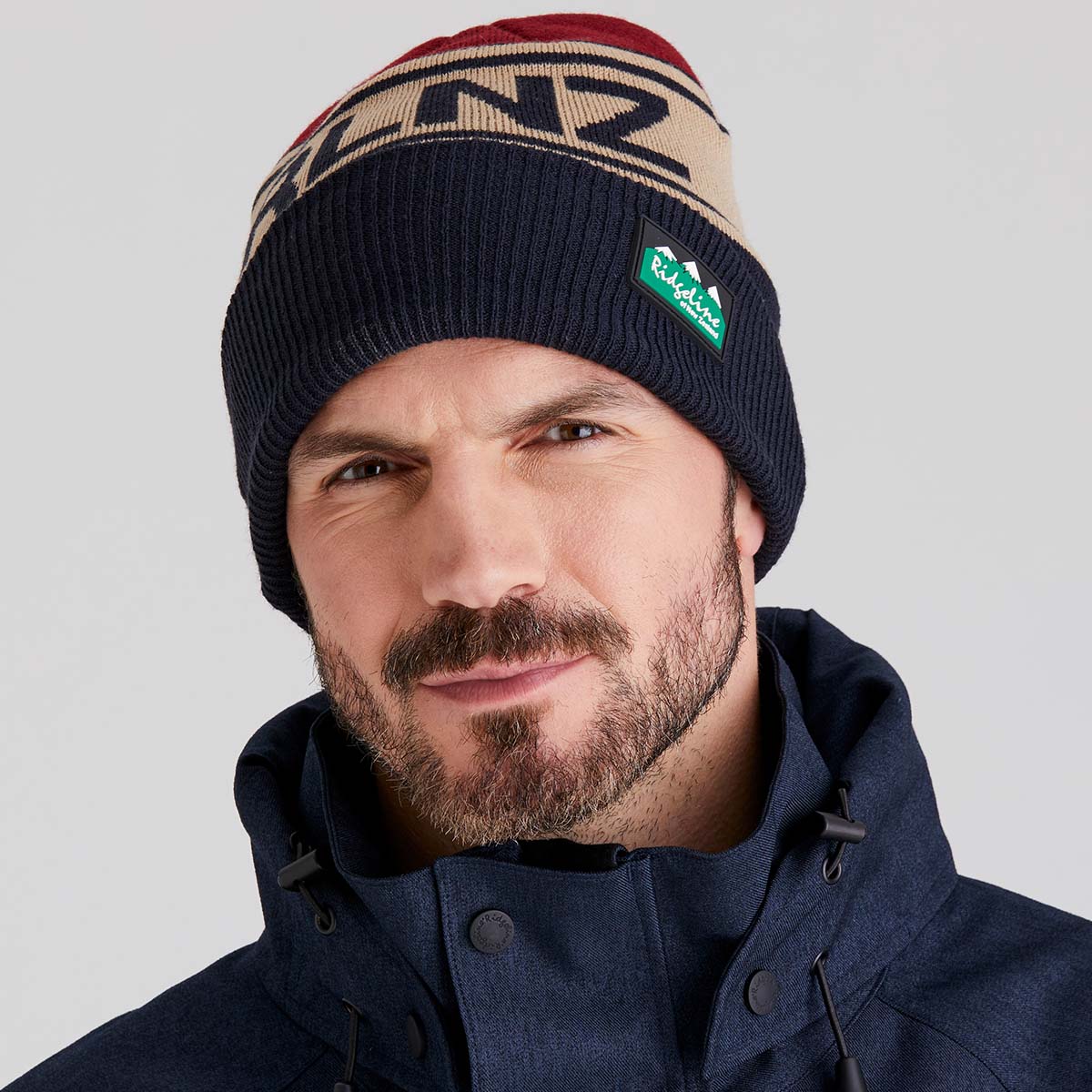 Man wearing a beanie with a brand logo on a gray background